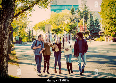 Diversité ethnique d'un groupe d'étudiants universitaires marcher et parler ensemble sur le campus à l'automne ; Edmonton, Alberta, Canada Banque D'Images