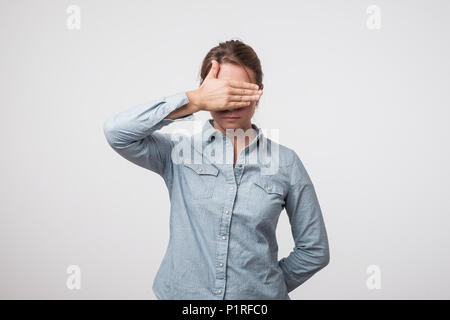 Jeune femme européenne en shirt cache sa face, studio photo isolé sur un fond gris. Elle est triste et honteux Banque D'Images