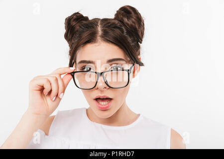 Gros plan Photo de surpris adolescente 20s avec double buns hairstyle et appareil dentaire touchant lunettes avec regard curieux sur bac blanc isolé Banque D'Images