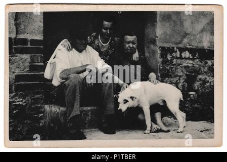 La République socialiste tchécoslovaque - circa 1960 : Retro photo montre les populations rurales s'asseoir sur la porte avec un chien. Photographie noir et blanc vintage Banque D'Images