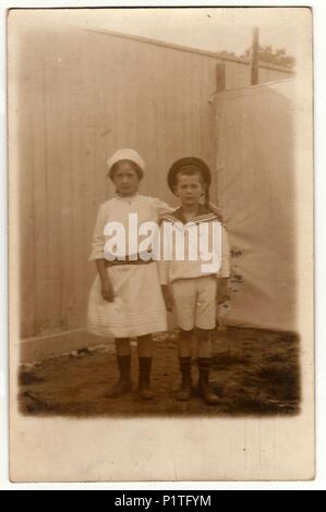 Hambourg, Allemagne (Deutsches REICH) - 13 NOVEMBRE 1917 : Vintage photo montre la fratrie (fille et garçon) posent dans la cour. Garçon porte un costume de marin et porte une robe blanche. Retro noir et blanc de la photographie. Banque D'Images