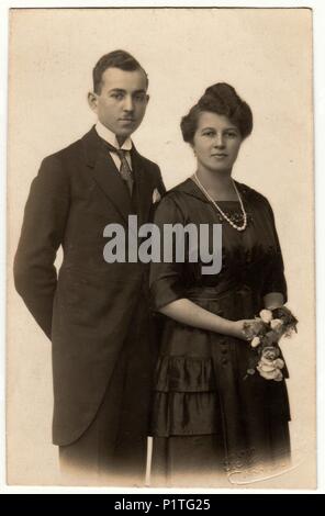 CHRASTAVA (KRATZAU), la République tchécoslovaque - VERS 1920 : Vintage photo montre un jeune couple porte des vêtements noirs. Femme fleurs. Retro noir et blanc de la photographie. Banque D'Images