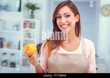 Cute young woman holding du pamplemousse dans la cuisine. En regardant la caméra. Banque D'Images