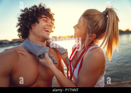 Belle jeune couple resting, souriant et serrant après une formation réussie par la rivière au coucher du soleil. Banque D'Images