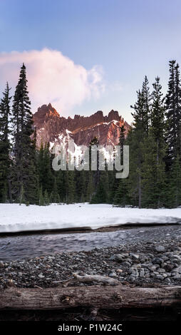 Scène de la forêt de montagne éclairé par le coucher du soleil avec la neige, les arbres et la rivière en premier plan Banque D'Images