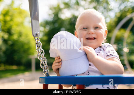 Bébé Garçon jouant dans un terrain de jeux. Portrait of smiling toddler looking at camera with happy face, plaisir. Le balancement sur journée ensoleillée à l'extérieur. Banque D'Images