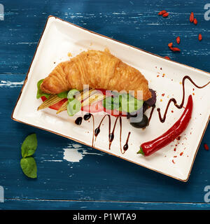 Sandwich appétissant avec des croissants et des légumes sur la plaque rectangulaire plat, bol d'olives et tomates cerises et baies de goji séchées sc Banque D'Images