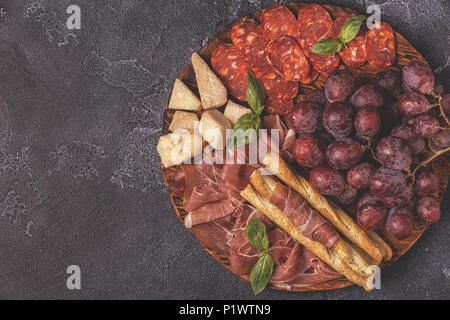 Jambon, saucisses, vin, raisin, le parmesan sur la table sombre, selective focus. Banque D'Images