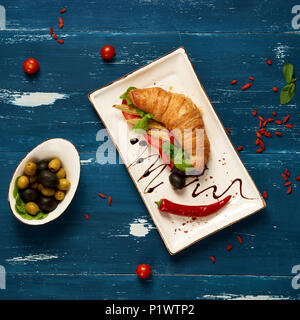 Sandwich appétissant avec des croissants et des légumes sur la plaque rectangulaire plat, bol d'olives et tomates cerises et baies de goji séchées sc Banque D'Images