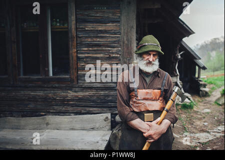 Old forester barbu avec ax près de cabane en bois Banque D'Images