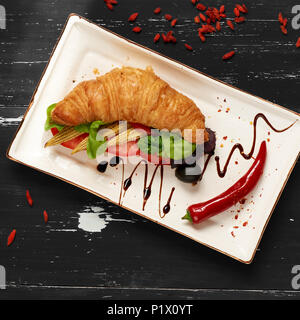 Sandwich appétissant avec des croissants et des légumes sur la plaque rectangulaire plat, bol d'olives et tomates cerises et baies de goji séchées sc Banque D'Images