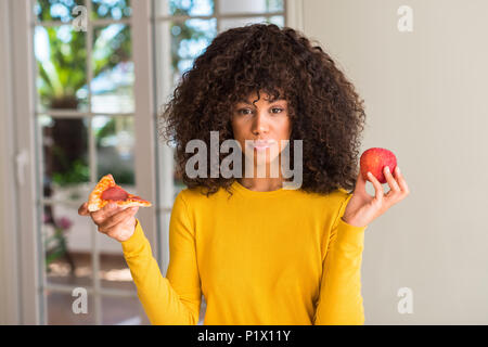 African American Woman choisir entre Apple et pizza slice avec une expression confiante face à la pensée intelligente grave Banque D'Images