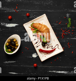 Sandwich appétissant avec des croissants et des légumes sur la plaque rectangulaire plat, bol d'olives et tomates cerises et baies de goji séchées sc Banque D'Images
