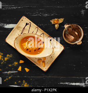 Soupe de potiron crémeux délicieux dans bol ovale et plaque rectangulaire debout sur bleu de table en bois. Restaurant appétissant repas vegan servi avec pain sl Banque D'Images