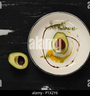 L'avocat coupé en deux demi-parties décorées avec le thym, la sauce jaune et les écrous de cèdre couché sur plaque ronde plate. Restaurant délicieux repas vegan pour les matières foo Banque D'Images