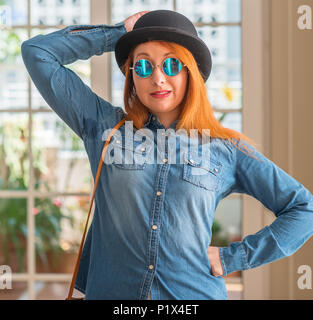 Rousse élégante femme portant chapeau melon et des lunettes de confondre et de s'interroger sur la question. Incertain avec le doute, la pensée avec la main sur la tête. Pensive c Banque D'Images