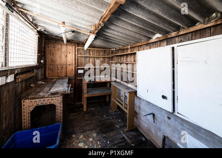 L'intérieur d'un vieux hangar abandonné avec des workbench, placards, étagères, toit de l'amiante et le dangereux. Banque D'Images