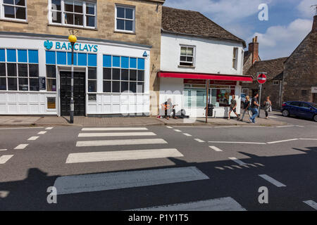 Un guitariste joue sur busker Malmesbury High Street, au début de l'été soleil, à côté d'un la Barclays Bank et un passage clouté, Wiltshire, Royaume-Uni Banque D'Images