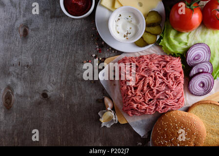 La viande hachée crue sur papier, les ingrédients pour burger avec la tomate, l'oignon et les assaisonnements sur fond de bois Banque D'Images