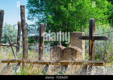 Ancien Nouveau Mexique cimetière avec des croix en bois et pierres tombales, une vieille échelle et de barbelés, de hautes herbes et d'arbres. Banque D'Images