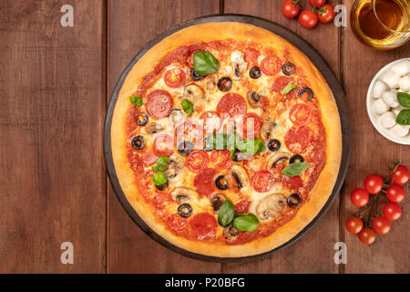 Photo prise à la verticale de la pizza au pepperoni, avec verre de vin blanc, tomates cerises et mozzarellini fromage, tourné à partir de ci-dessus sur fond rustique foncé avec pl Banque D'Images