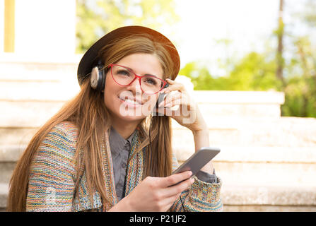 Belle fille de l'adolescence à écouter la musique sur un téléphone intelligent assis sur les escaliers dans le parc urbain Banque D'Images