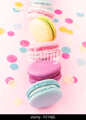 La rangée verticale de macarons colorés sur fond rose décoré de confettis. Banque D'Images