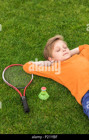 Portrait de petit garçon reposant sur pelouse verte et de l'équipement à proximité de badminton par Banque D'Images