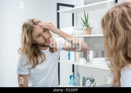 Beau jeune homme aux cheveux long sur la face de la peau contrôle dans la salle de bains Banque D'Images