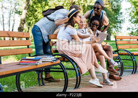 Groupe multiculturel d'étudiants à l'aide de tablet alors qu'elle repose sur le banc dans le parc Banque D'Images