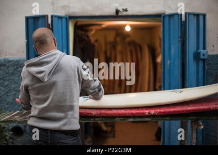 Le Maroc, Taghazout, man waxing his surfboard Banque D'Images