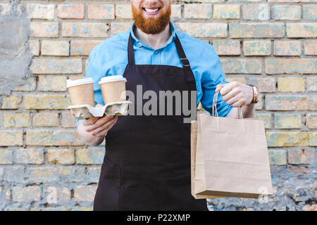 Cropped shot of male tablier barista en tenant les sacs en papier et des gobelets jetables avec café Banque D'Images