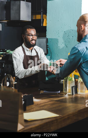 Cropped shot of african american barista tasse de café donnant aux jeunes barbus client en cafe Banque D'Images