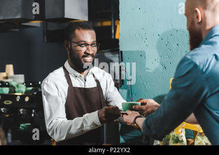 Cropped shot of african american barista tasse de café donnant à client barbu in coffee shop Banque D'Images