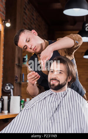 Heureux jeune homme se coupe de coiffure professionnel au salon de coiffure Banque D'Images