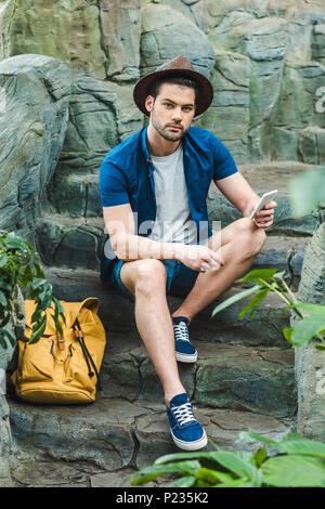 Young man using smartphone tout en étant assis sur un escalier en pierre Banque D'Images