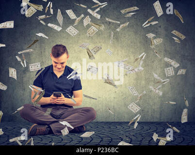 Jeune homme assis et using smartphone gagner énorme somme d'argent dans Internet. Banque D'Images Jeune homme assis et using smartphone gagner énorme somme d'argent dans Internet. Banque D'Images