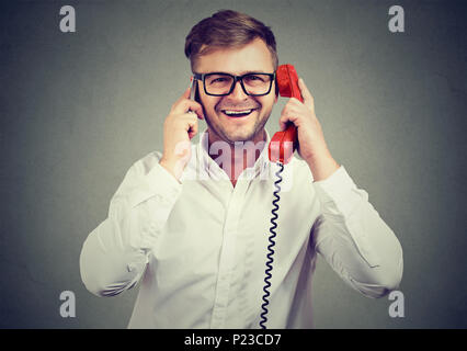 Beau jeune homme parlant à la fois sur le téléphone rouge à l'ancienne et nouveau smartphone étant occupé. Banque D'Images