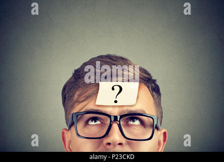 Jeune homme portant des lunettes noires avec un point d'interrogation sur le front à la recherche. Banque D'Images