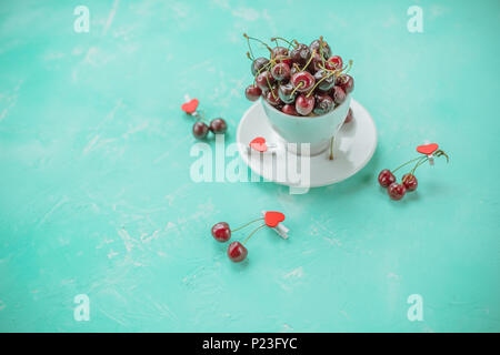 Tasse blanche avec les baies mûres de cerise rouge et de plusieurs baies à l'avant de la cuvette. Composition sur un fond vert, l'émeraude. Le style de vie sain.Copy space Banque D'Images