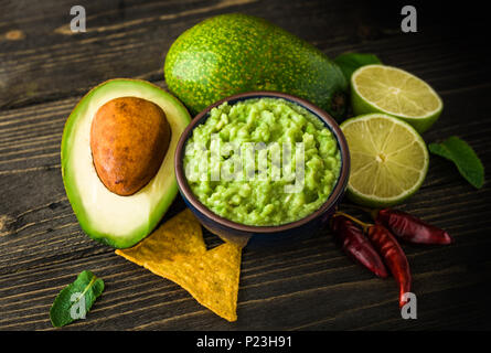 Le guacamole dans bol bleu avec des croustilles et de citron sur le bureau en bois. Banque D'Images