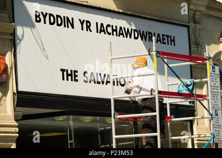 Un signpainter peinture l'Armée du Salut nom , au-dessous de la version galloise Byddin Iachawdwriaeth - Y - à l'extérieur d'un magasin de vêtements de bienfaisance, Aberystwyth Wales UK Banque D'Images