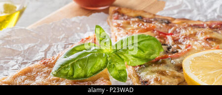 Deux morceaux de pizza aux champignons et fromage et aussi avec les tranches de citron et les feuilles de basilic sur une planche en bois recouverte de papier cuisson, servi avec Tom Banque D'Images