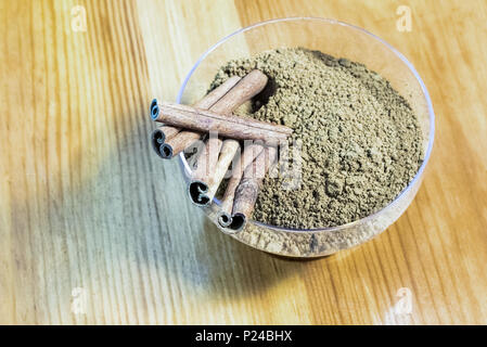 Poudre et les bâtons de cannelle dans un bol en verre sur fond de bois Banque D'Images