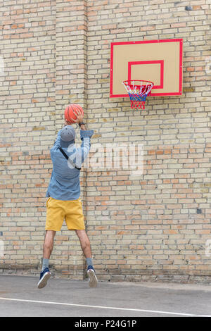 Vue arrière du jeune homme jouant au basket-ball seul Banque D'Images