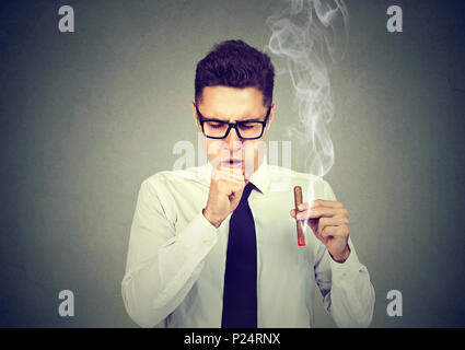 Homme fumant un cigare et la toux isolé sur fond gris Banque D'Images