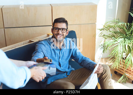 Cropped shot of smiling man holding newspaper et payez par carte de crédit dans cafe Banque D'Images