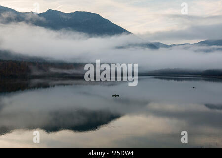 Un bateau de pêche au milieu de Sylvenstein lac dans la brume matinale. Bad Tölz-Wolfratshausen, Bavière, Allemagne. Banque D'Images