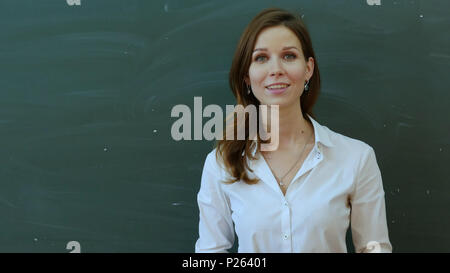Jeune femme heureuse de parler à l'enseignant permanent classe contre green board Banque D'Images