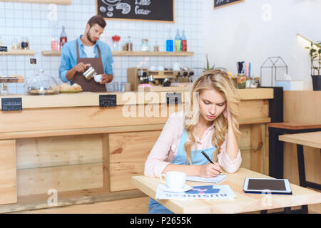 Les jeunes sérieux cafe owner notes pendant que barista travaillant derrière Banque D'Images